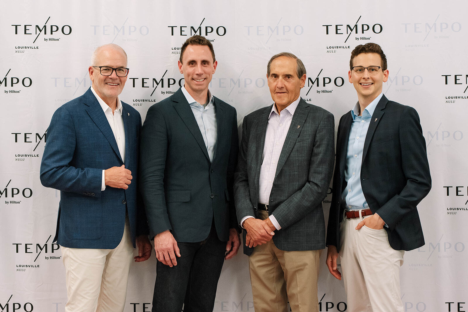 Four Men standing in front of a Tempo by Hilton Step & Repeat background